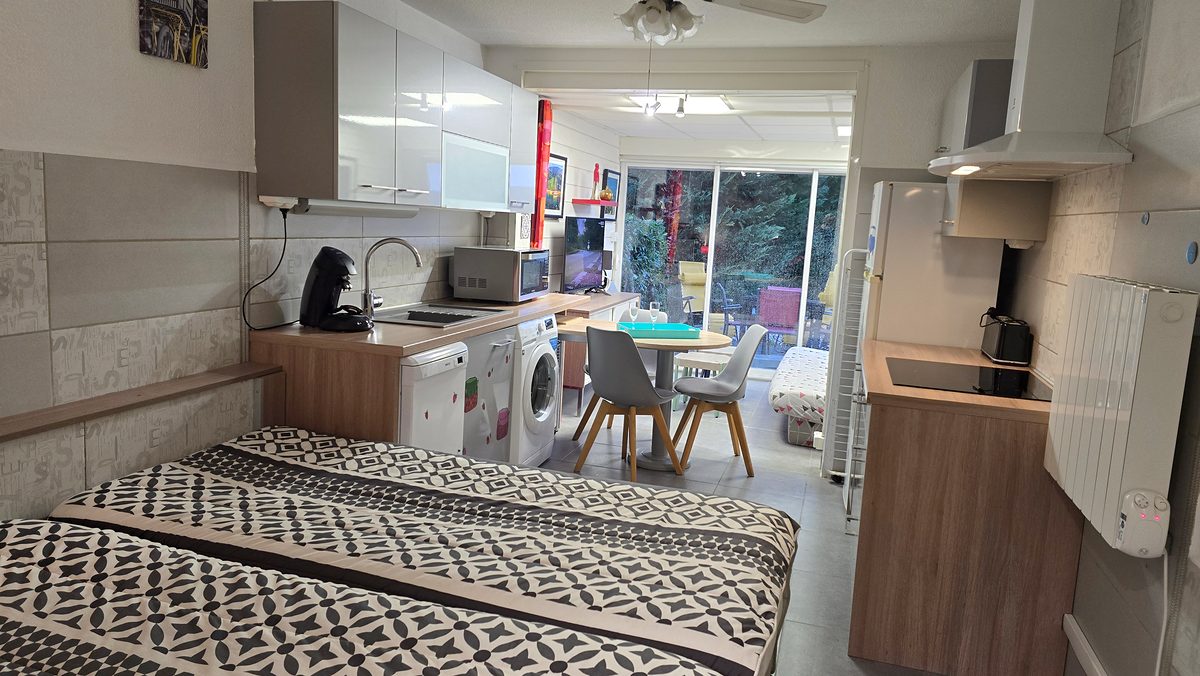 Vue d’ensemble du studio depuis les lits&nbsp;: cuisine, coin repas et loggia donnant sur le jardin